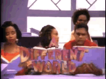 Group of women holding a large sign that reads 'Different World' in colorful letters, gathered in a room with purple walls and large window.