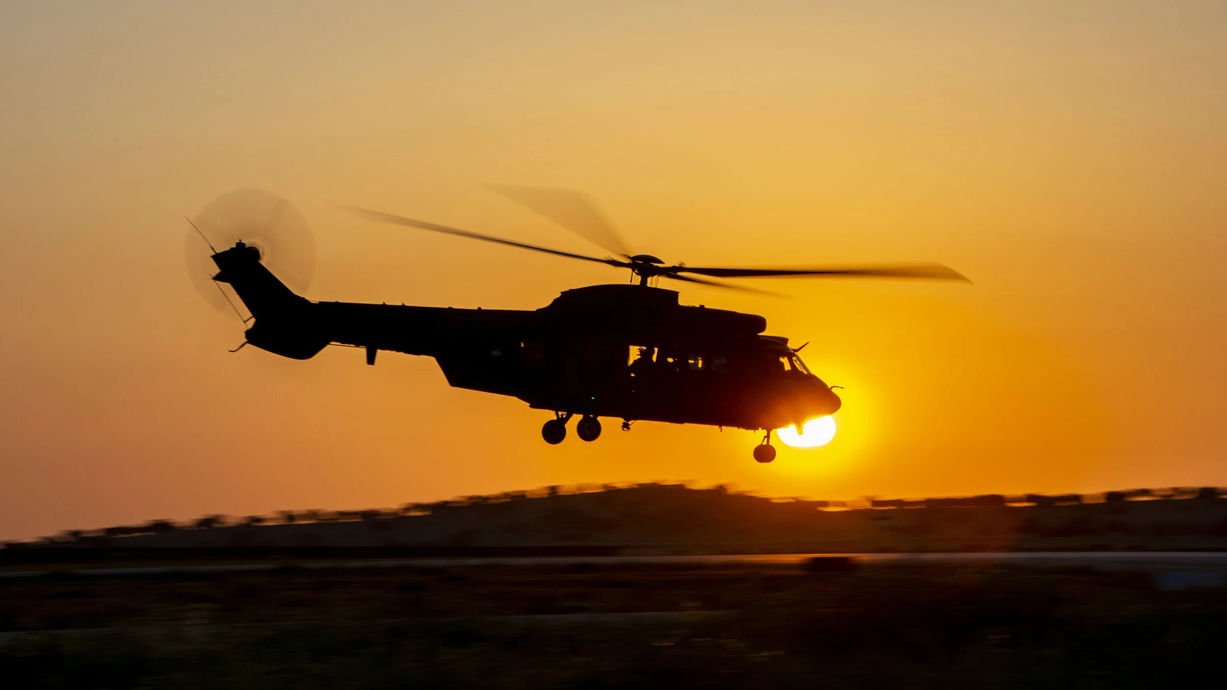 Silhouette of a helicopter flying at sunset.