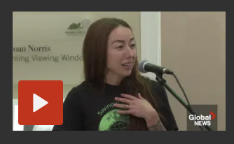 A woman speaking at a microphone during a press event or interview, with a banner in the background.