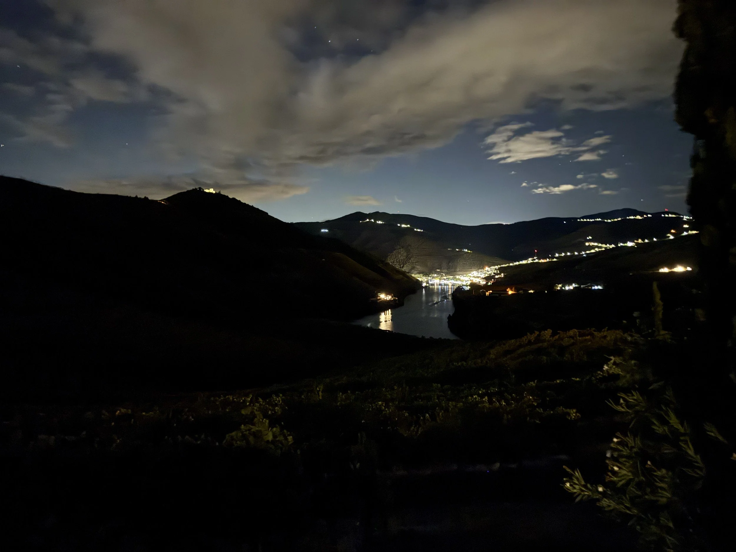 Village lights reflected in the Douro River at night below dark hills.