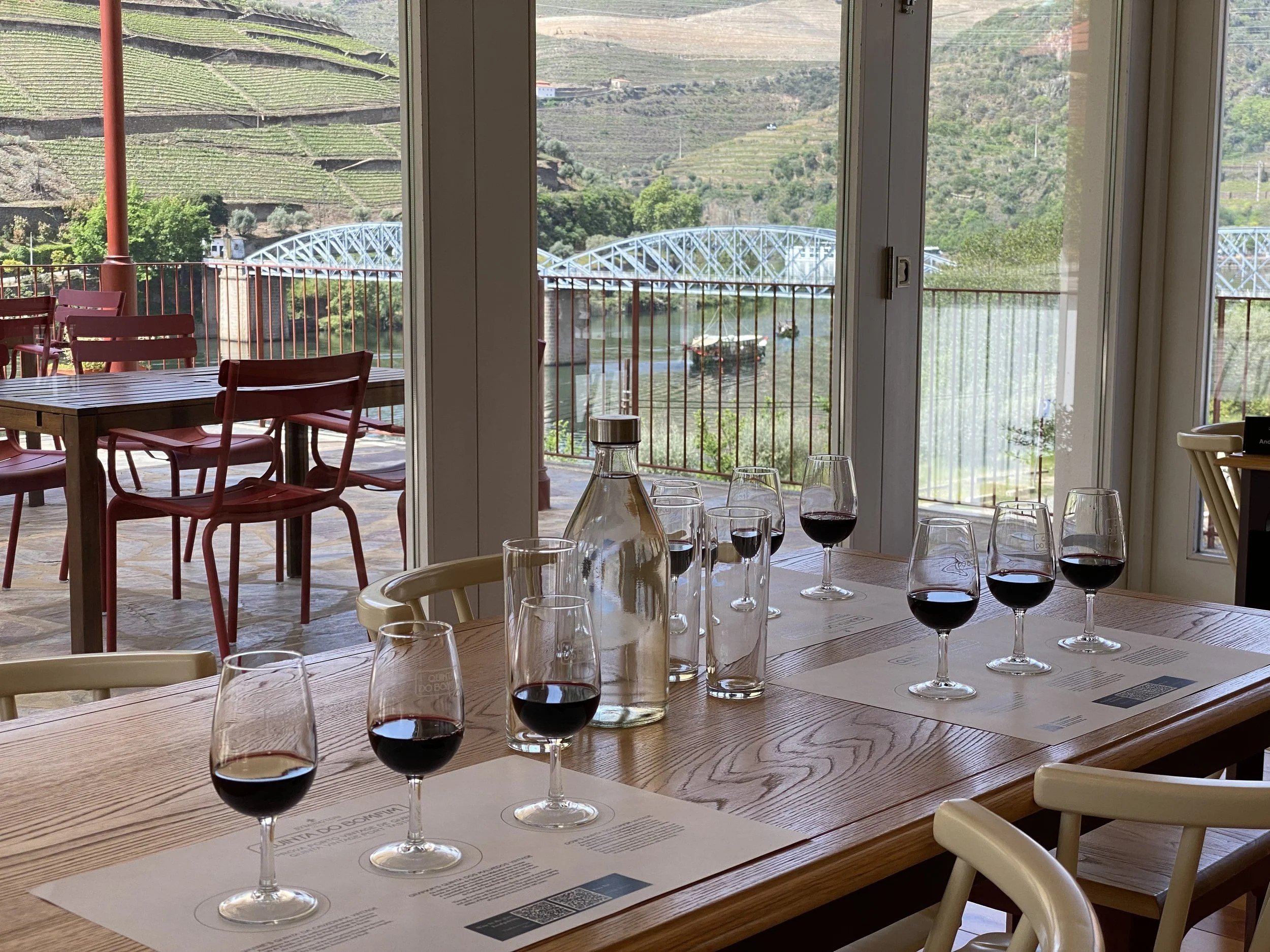 Port glasses set out for a tasting at Quinta do Bomfim, with the Douro and the Pinhão bridge beyond.