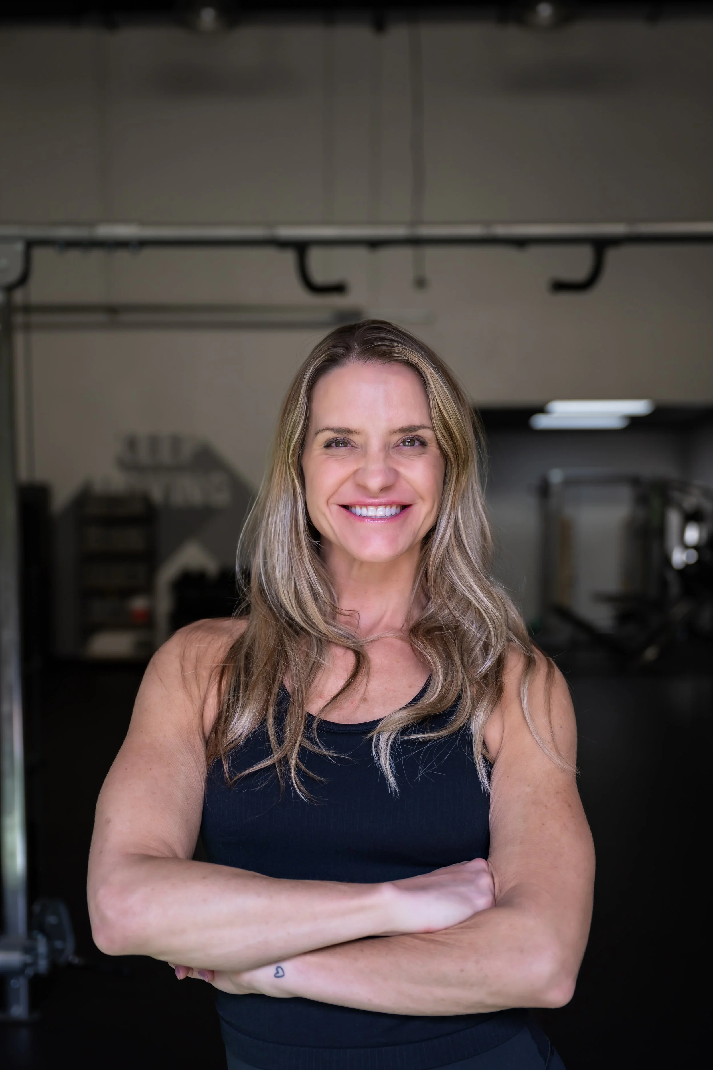 A woman smiling, with her arms crossed with a gym in the background