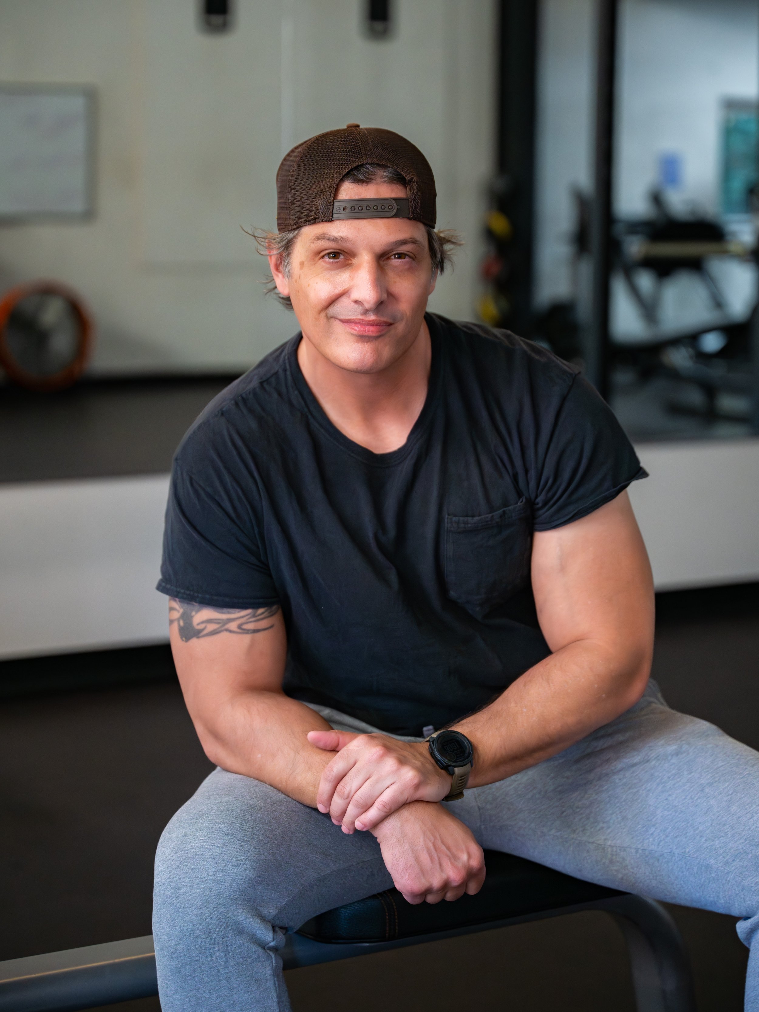 man with black shirt and hat on backwards sitting on a chair