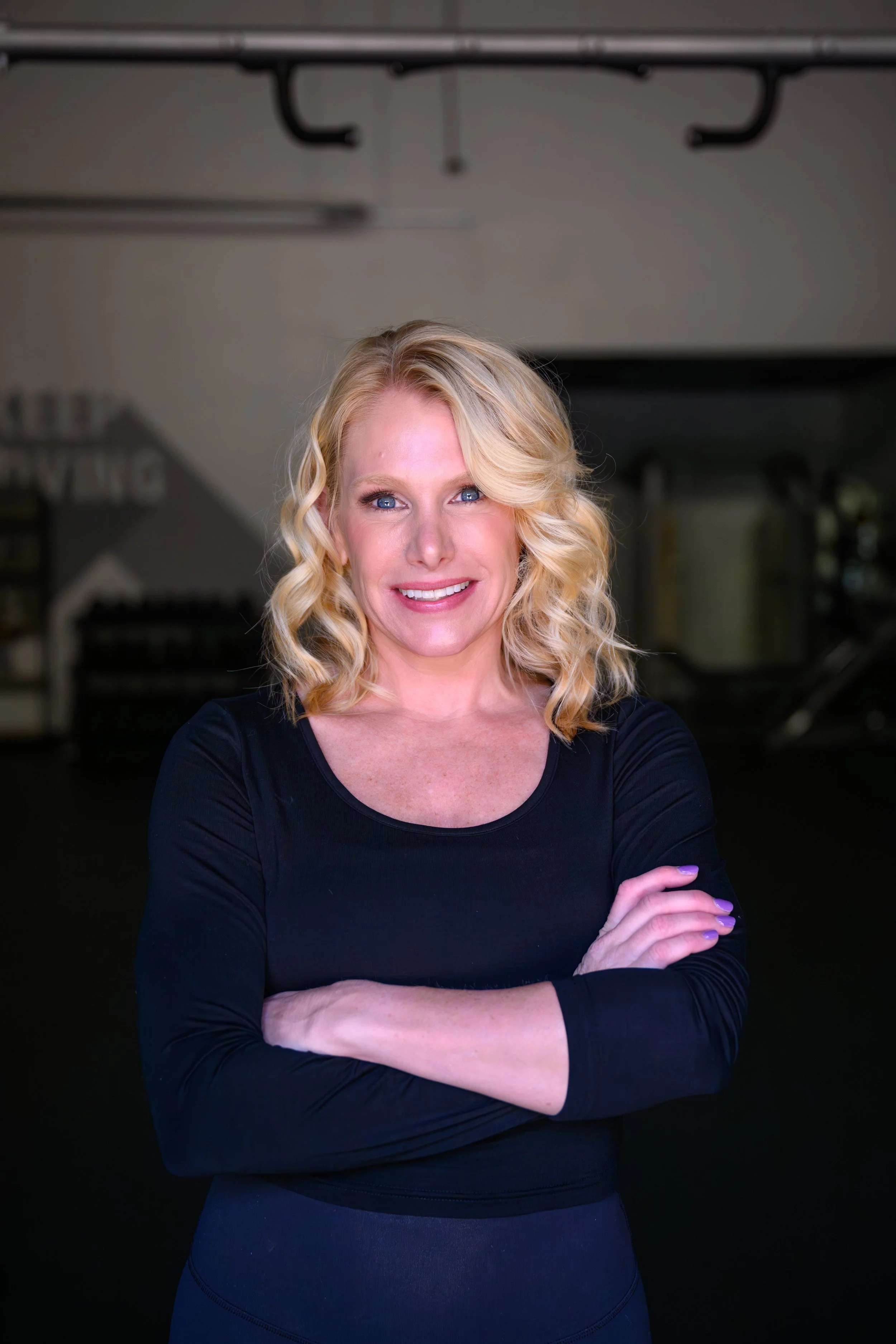 A woman with blonde hair smiling, wearing a black top, against a plain white background.