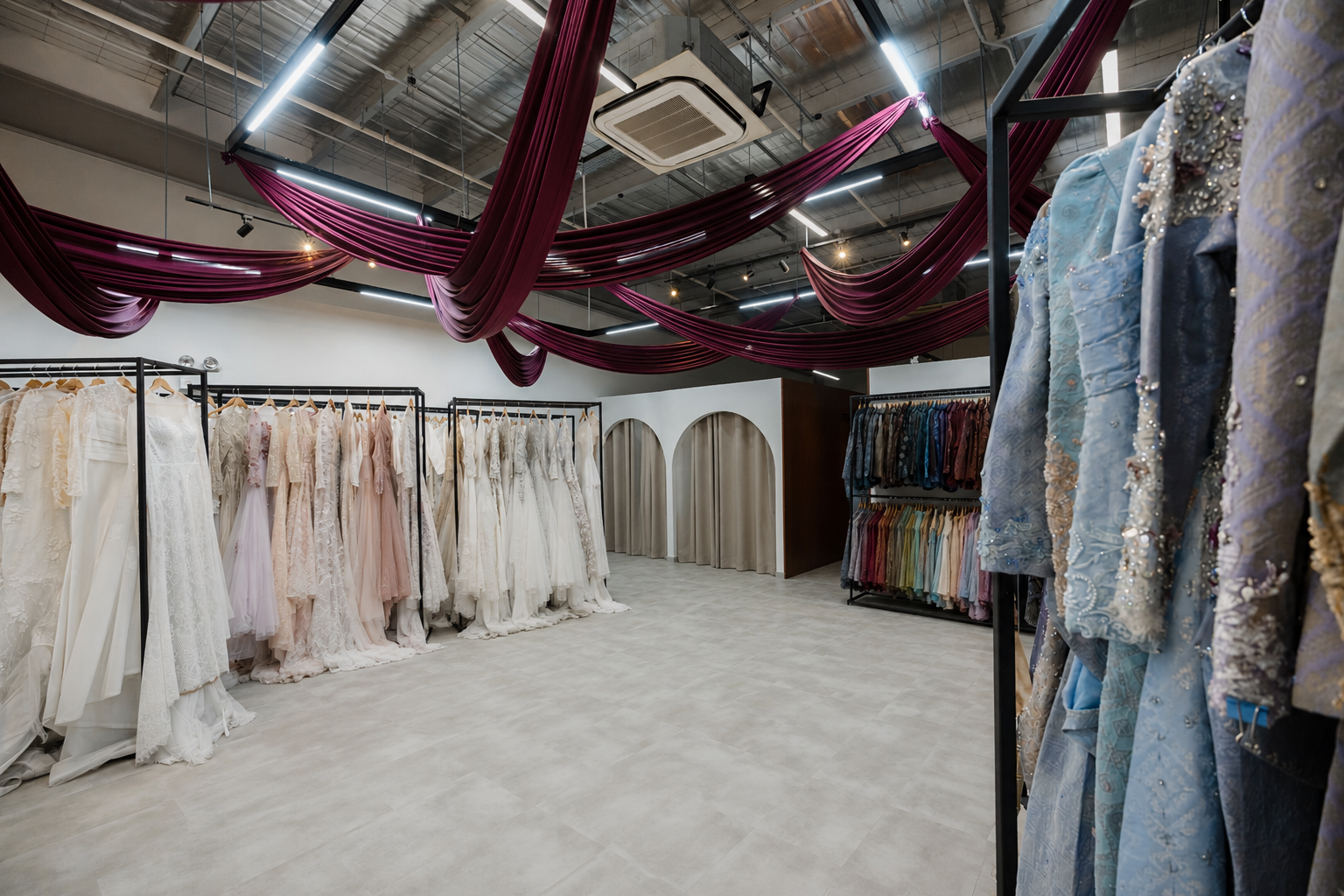 A bridal dress shop with mannequins wearing wedding gowns on black racks on the left and dresses in various colors on racks on the right, under red swaged fabric drapes hanging from the ceiling with modern LED lighting.