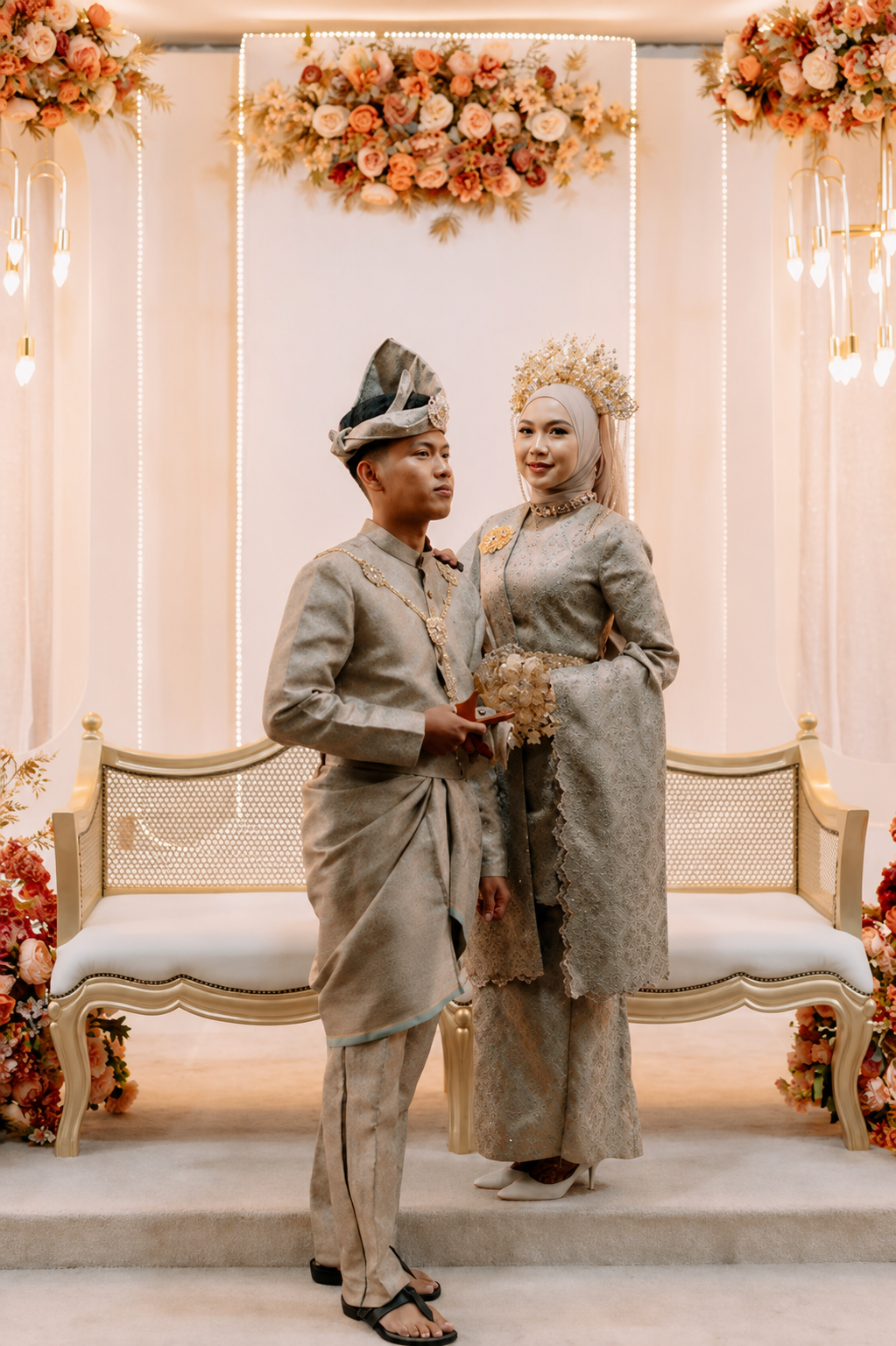 A couple dressed in traditional Indonesian wedding attire posing in front of floral wedding backdrop.