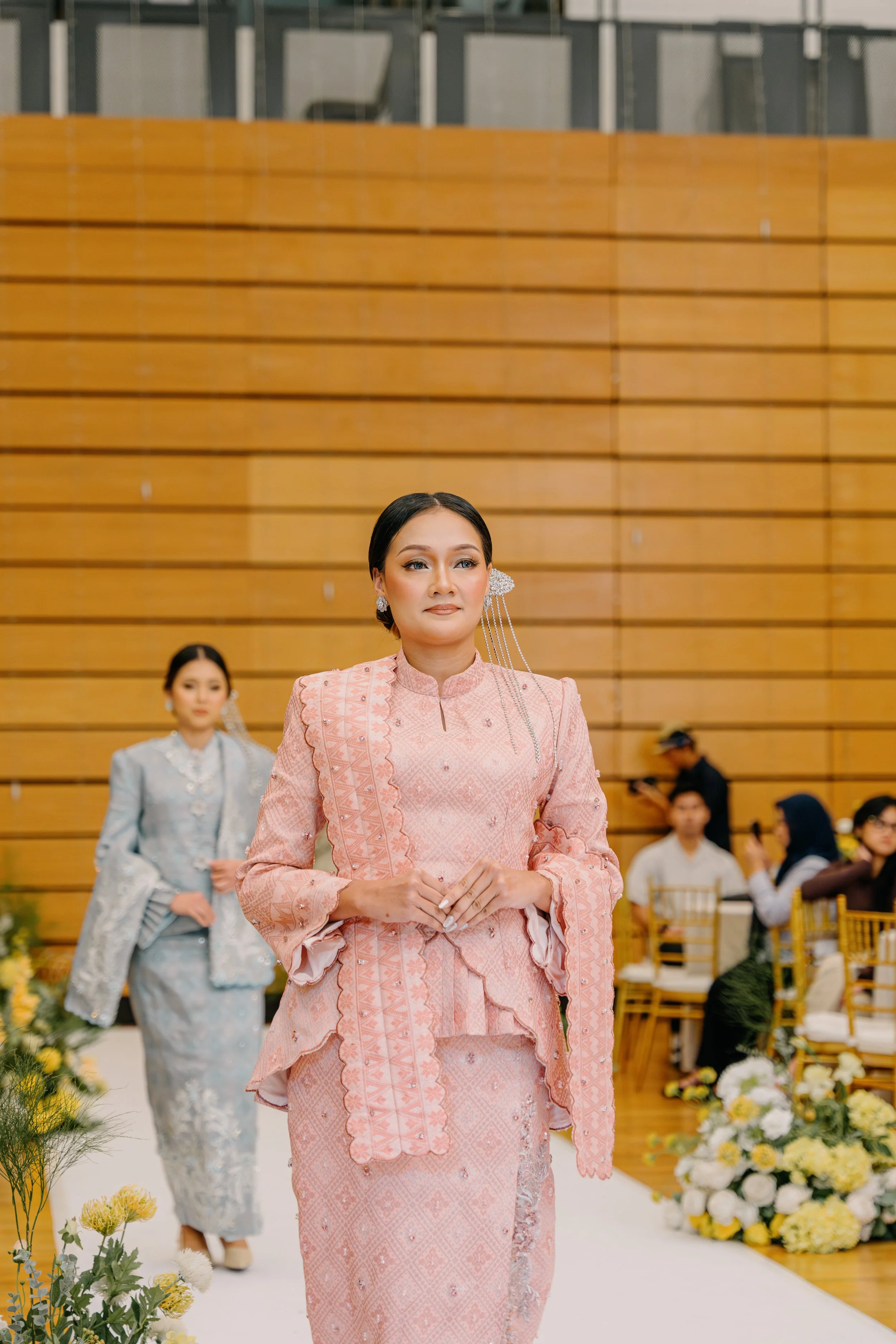 Women in traditional attire walking down the aisle during a wedding ceremony.