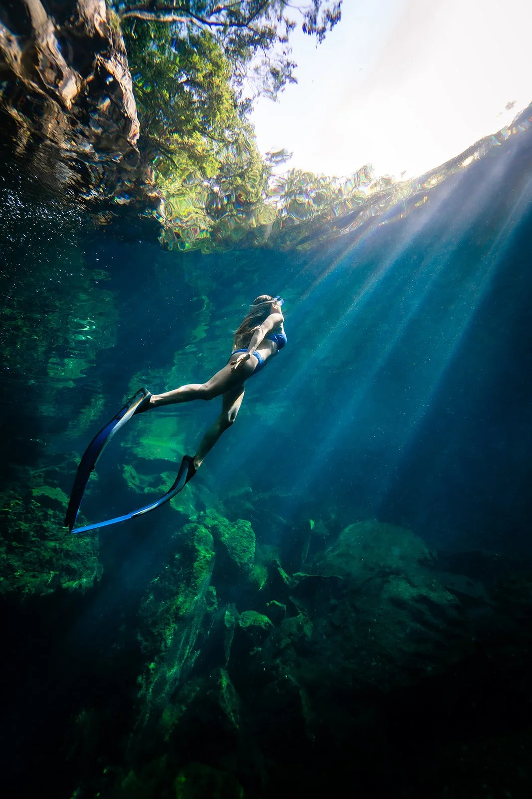 A woman doing free diving with blue  bikini and blue fins for an underwater photoshoot in a cenote