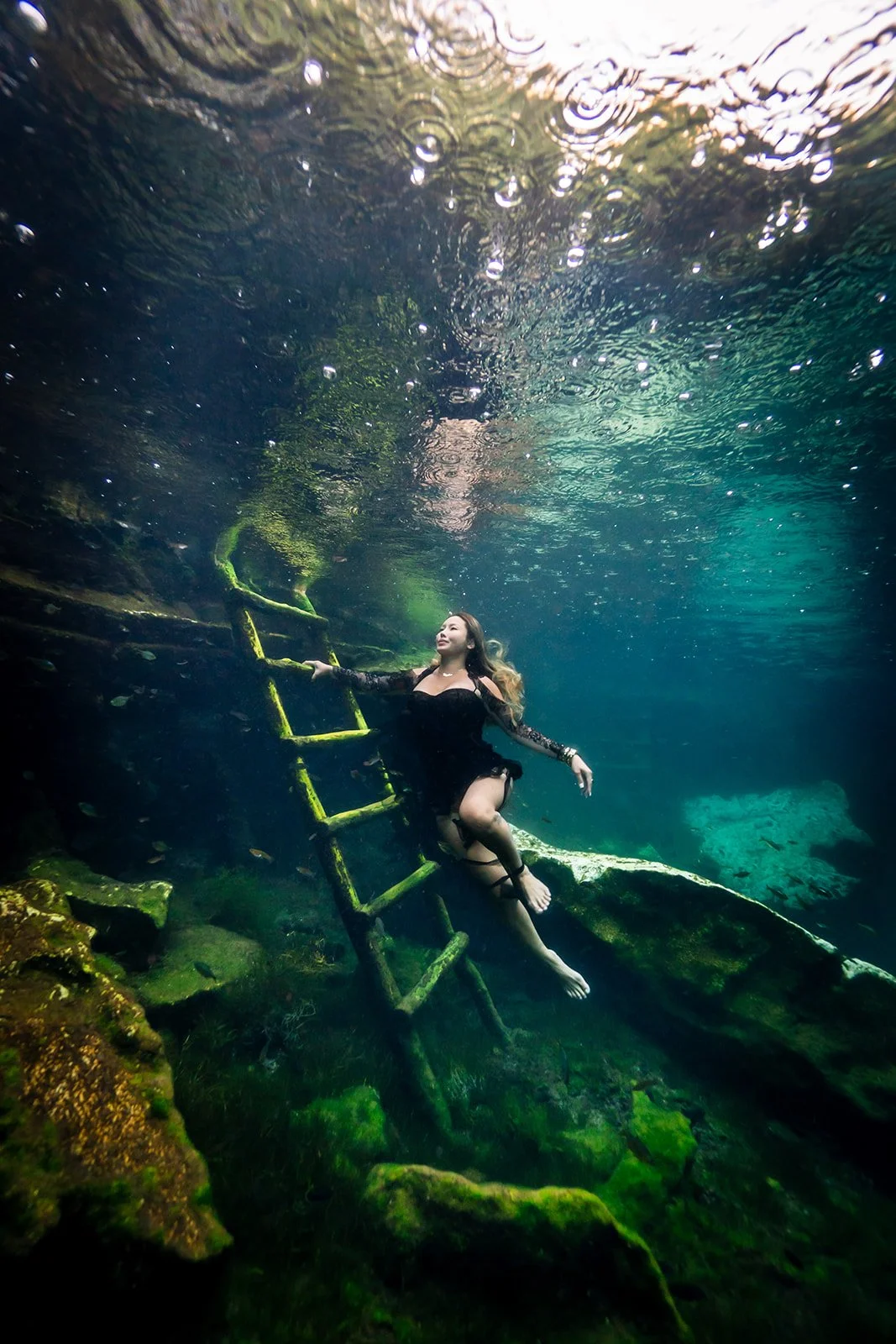 A woman posing in a black dress for an underwater photoshoot in a cenote close to Tulum