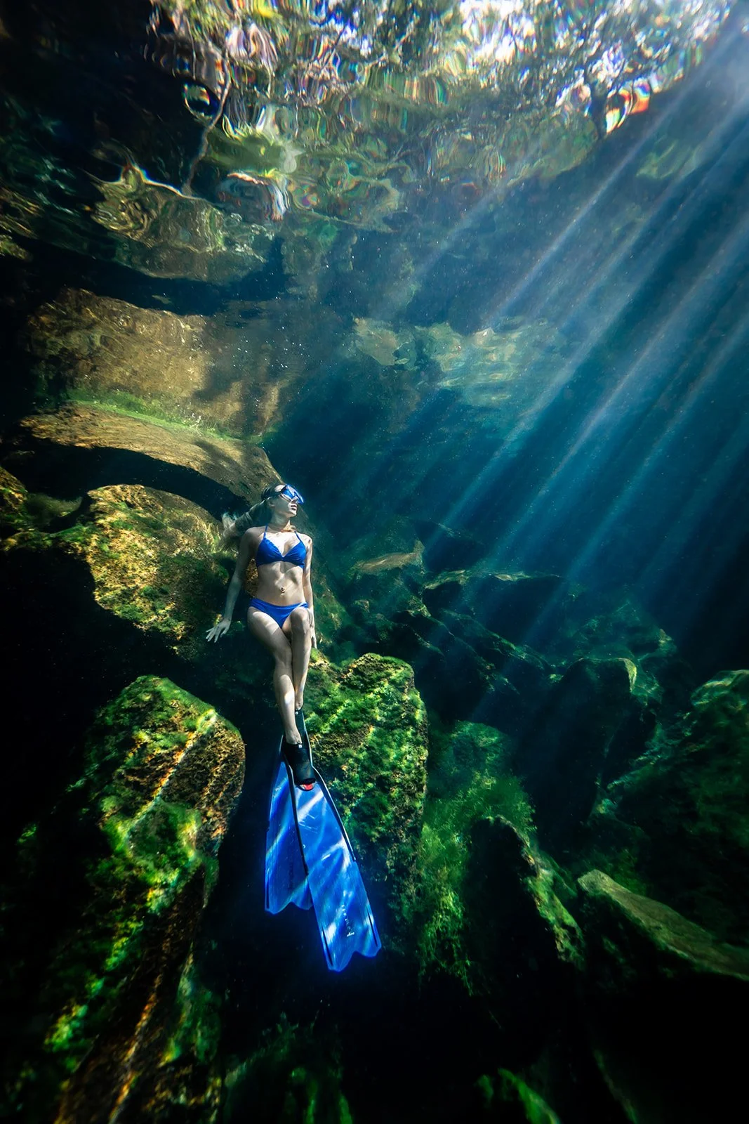 A woman sitting underwater posing for a portrait in a cenote near tulum