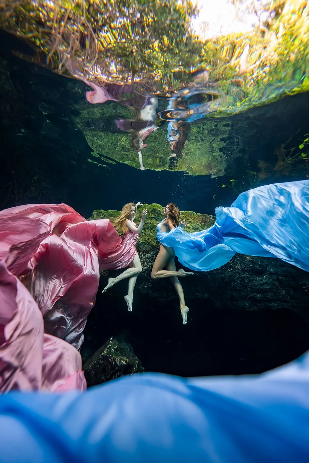 Two ladies modeling with a blue and a pink flying dress underwater in a cenote close to Cancun