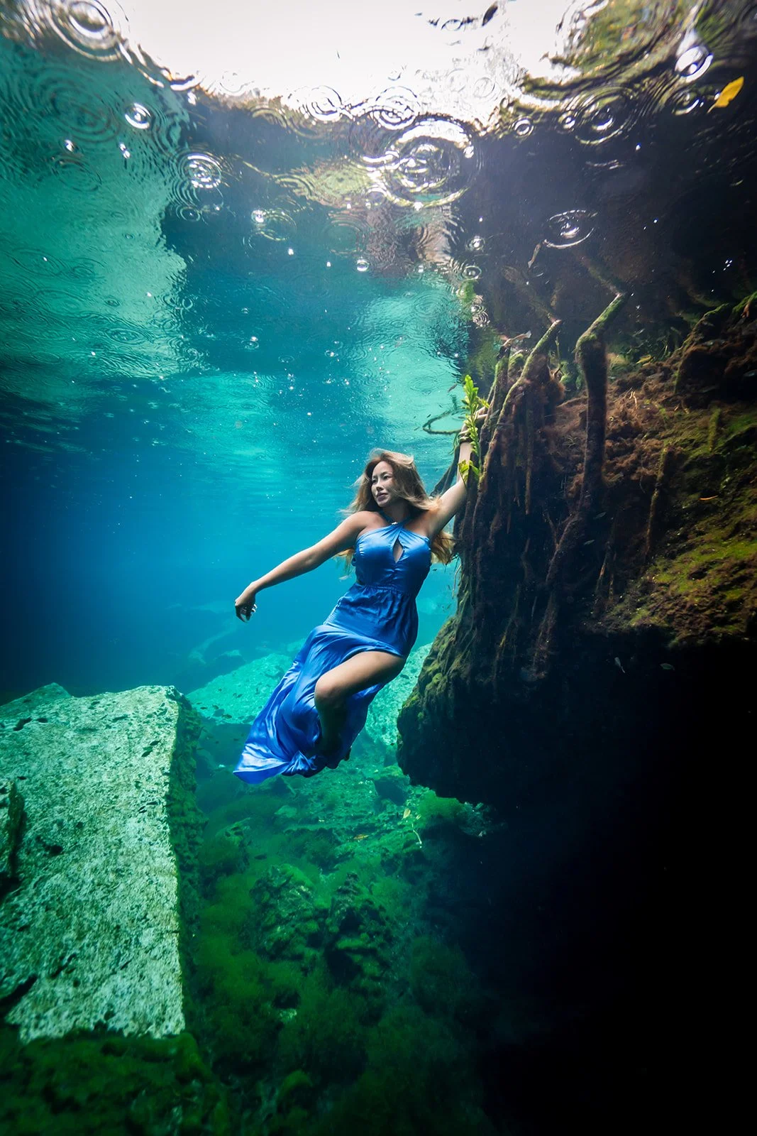 An Asian woman posing in a blue dress for an underwater photoshoot in a cenote between Tulu, and Playa del Carmen