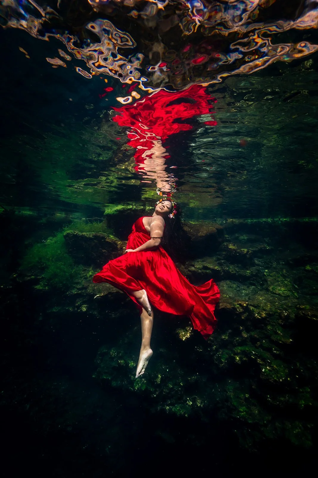A pregnant woman posing for a Maternity underwater photography session in Riviera Maya in a red dress