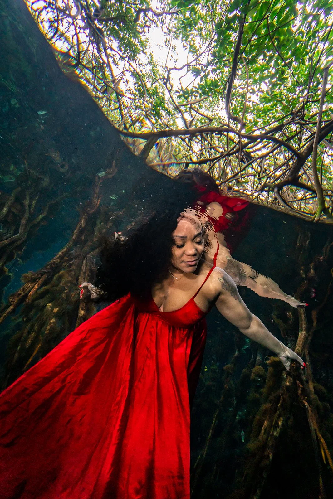 An African American woman posing in a red dress for an underwater photoshoot in a cenote close to Playa del Carmen