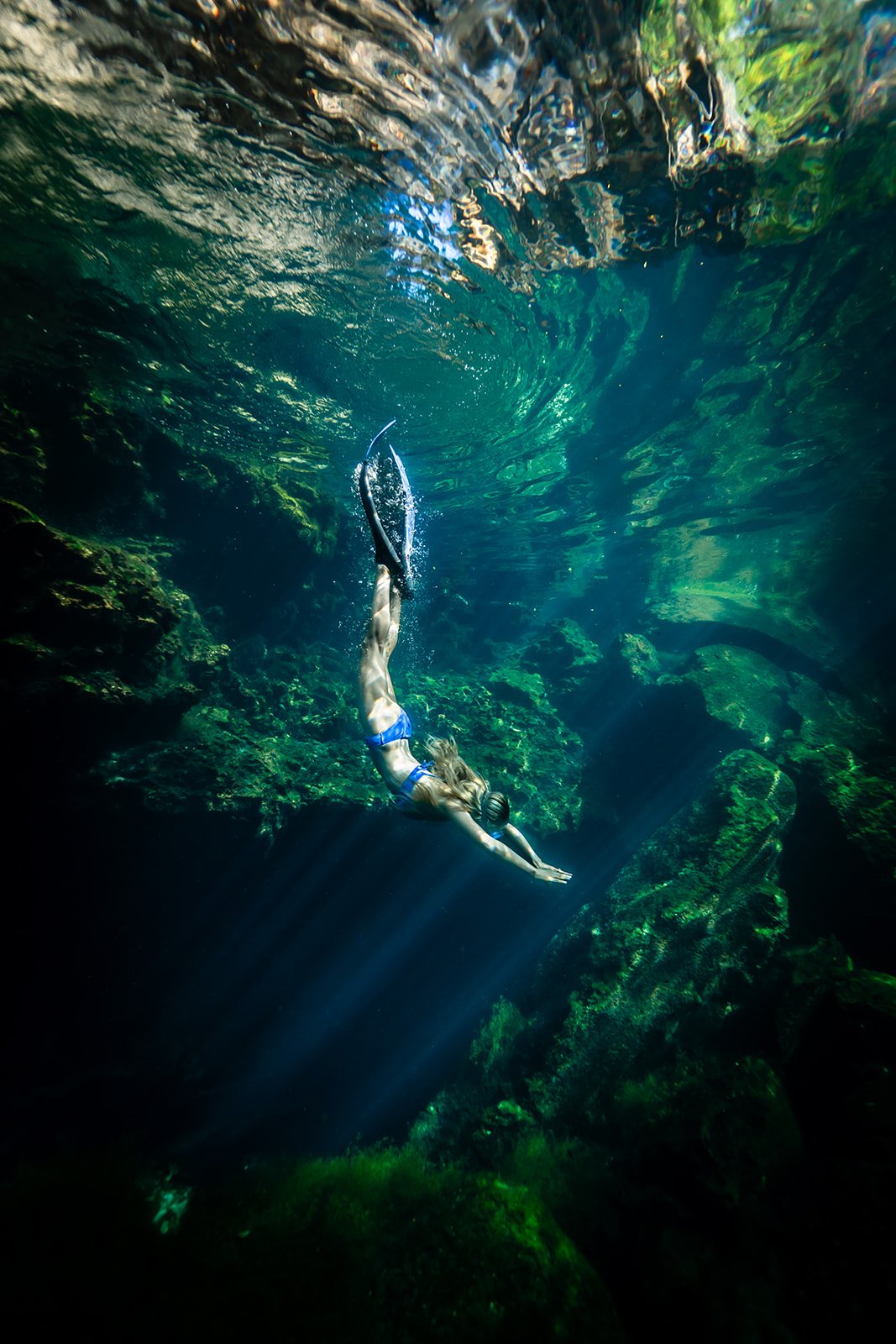 A woman diving in a blue bikini in a crystal clear cenote in Riviera Maya
