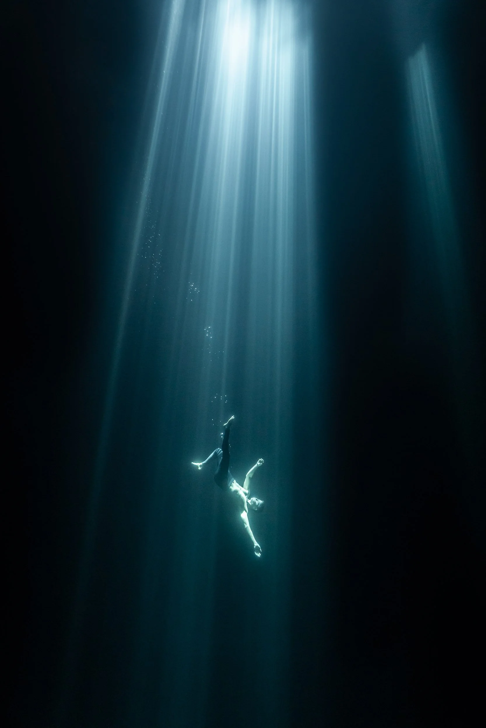 Person underwater, illuminated by beams of light.
