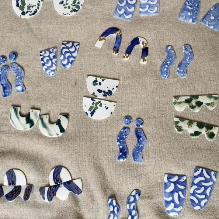 Assorted mosaic tiles with blue, green, and white patterns arranged on a beige fabric background.
