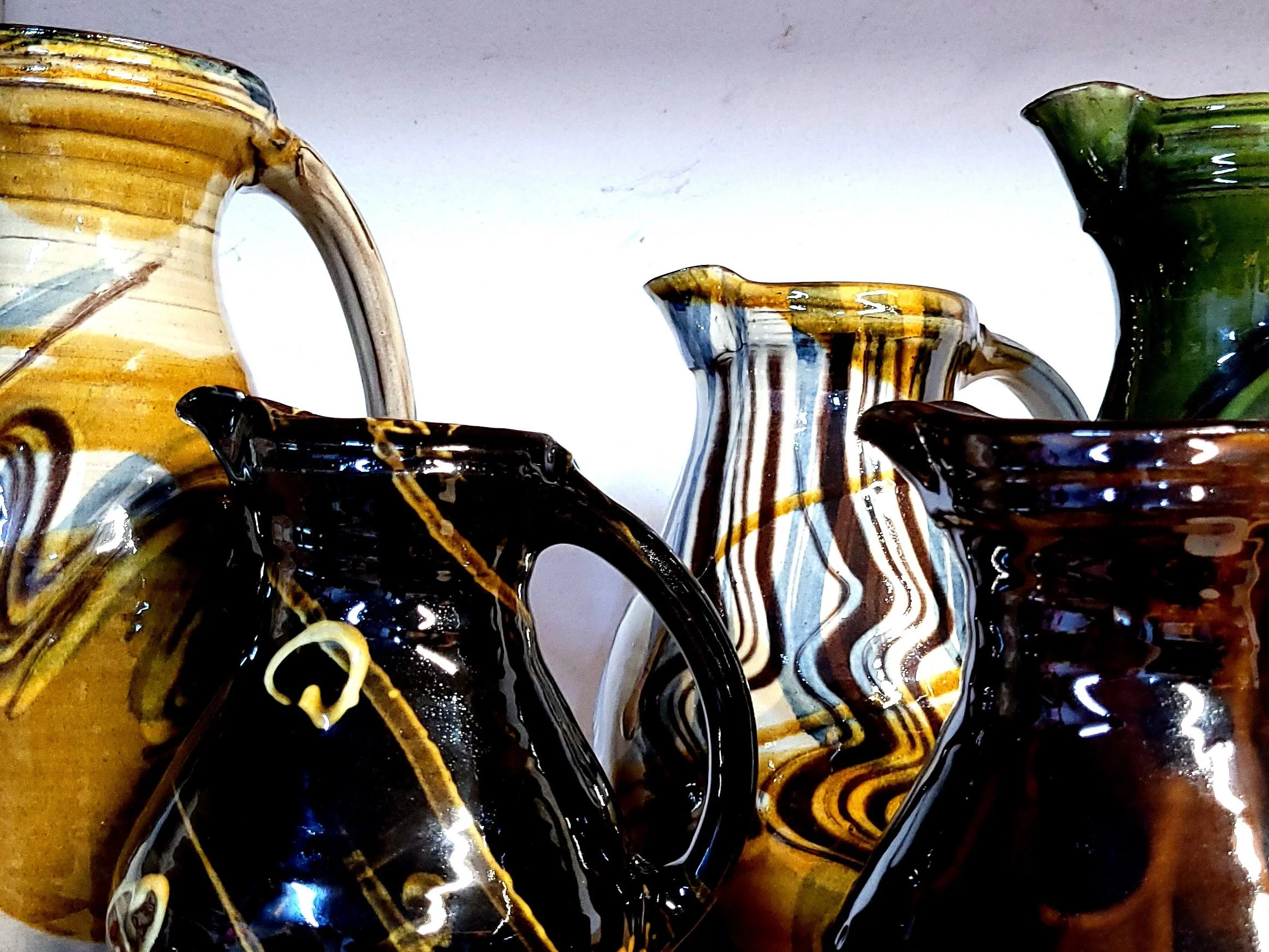 Close-up of colorful glass vases with swirling patterns of yellow, black, white, green, and brown on a white background.
