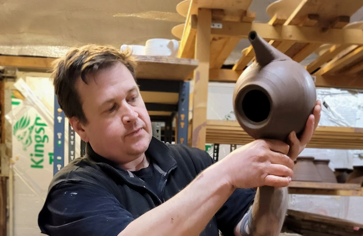 Man inspecting a brown ceramic jug in a workshop.