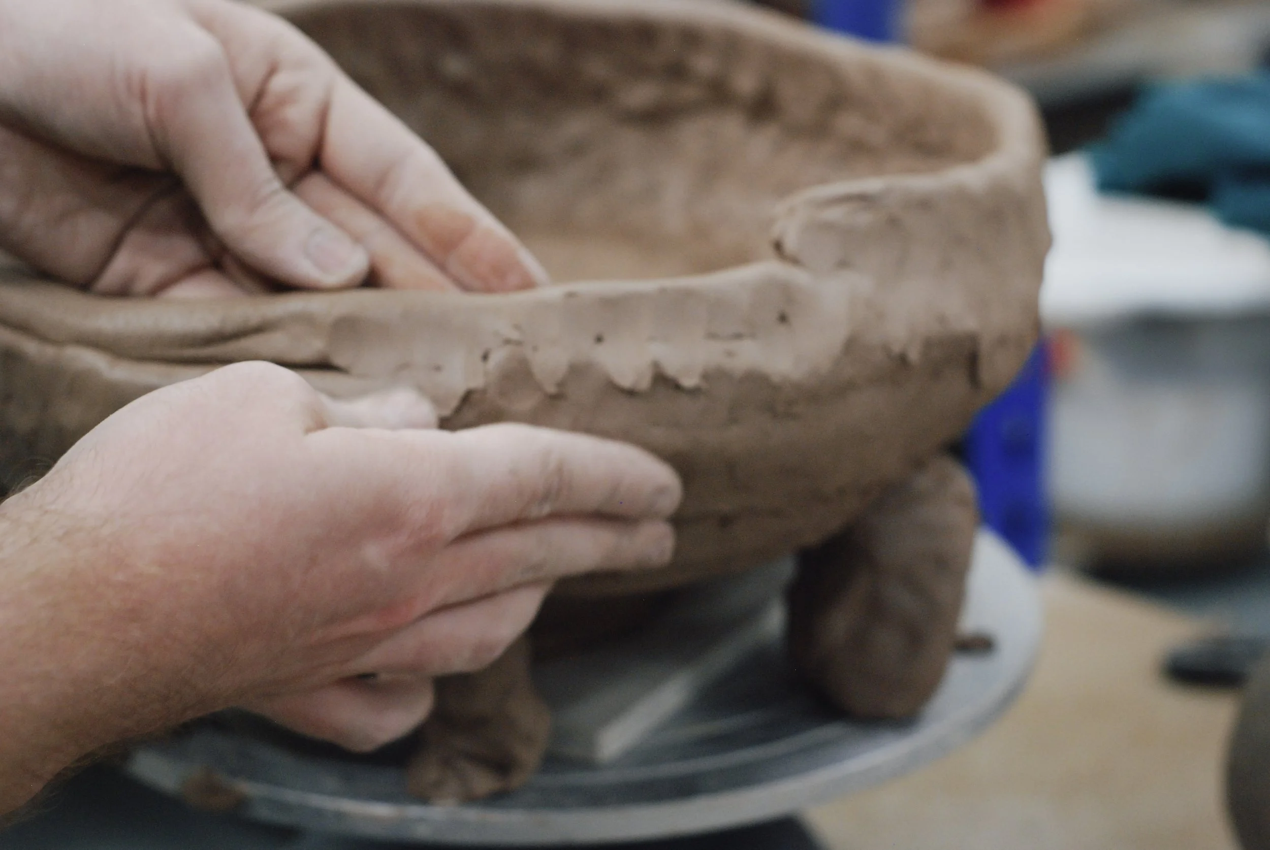 People shaping and smoothing a large clay sculpture or pottery piece with their hands