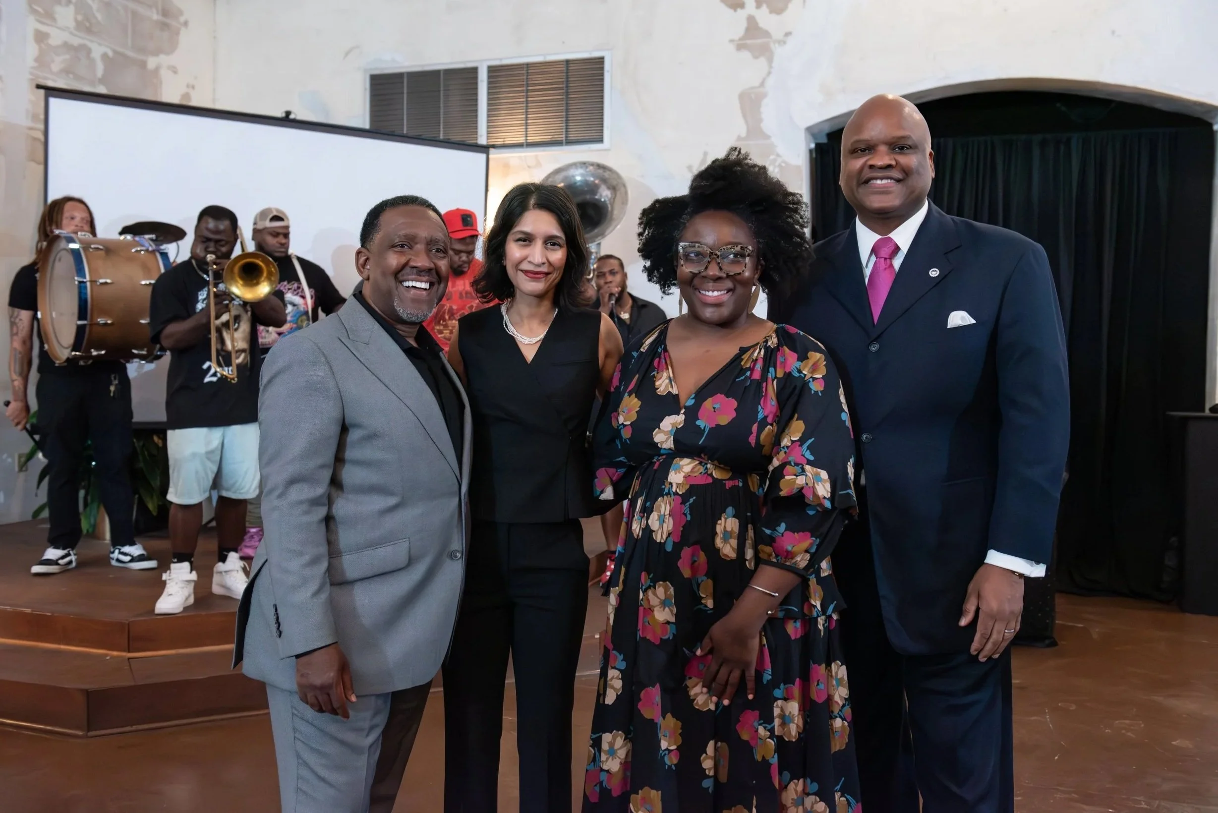 Four adults standing together smiling at an event, with a band playing in the background.