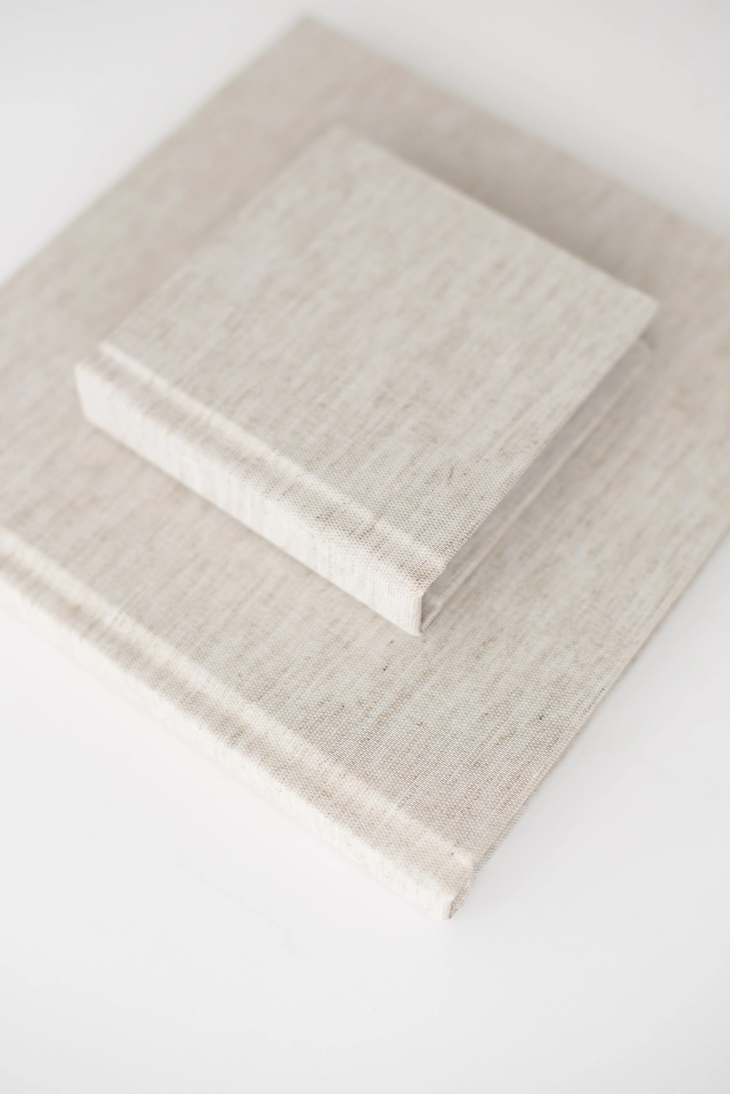 Two beige, linen-covered books stacked on a white surface.