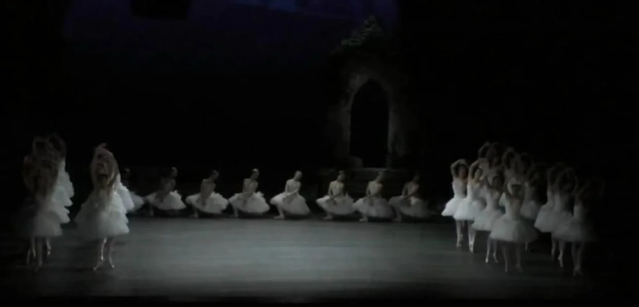 The swan students are now kneeling in a horizontal row across the back of the stage. On either side, the adult corps execute academic steps worthy of George Balanchine’s “Concerto Barocco”: here, relevé fifth position for feet, legs and arms. First …