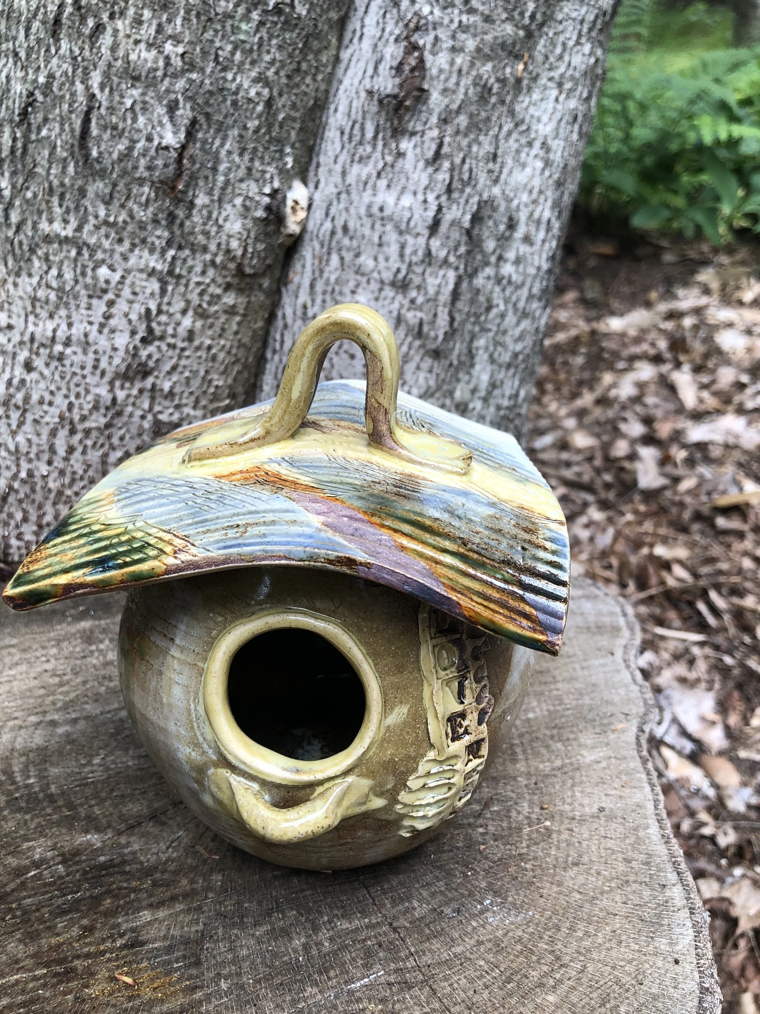 Decorative ceramic birdhouse with loop handle for hanging.