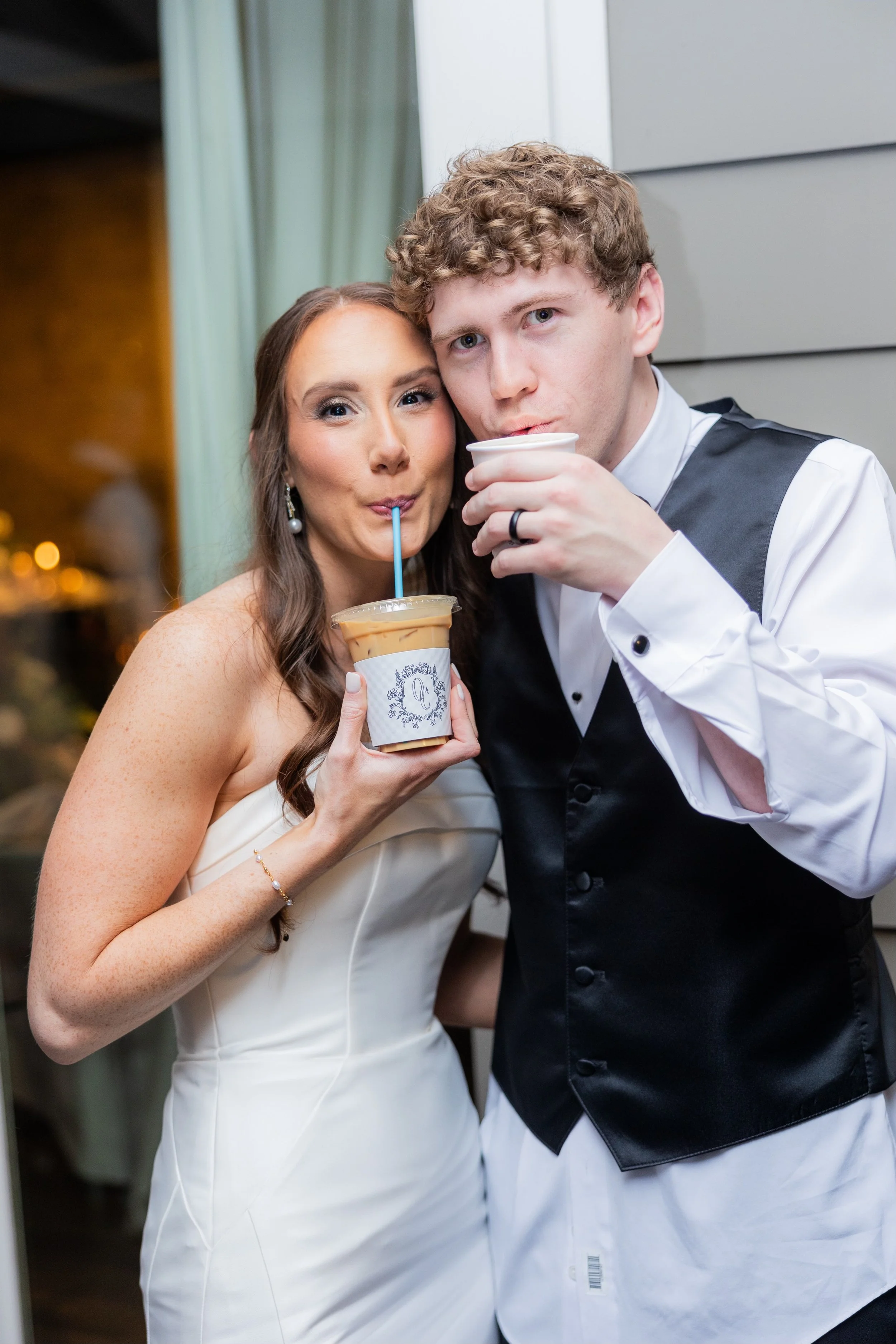 A couple dressed in wedding attire drinking beverages at a celebration.