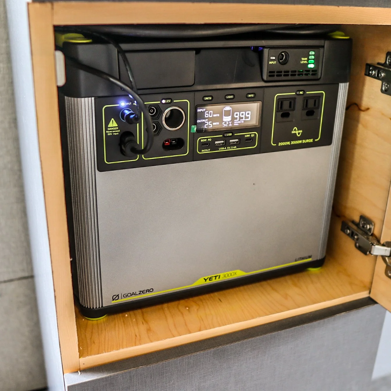 Portable power station placed on a wooden shelf inside a cabinet, with various ports and a digital display showing charging and battery information.