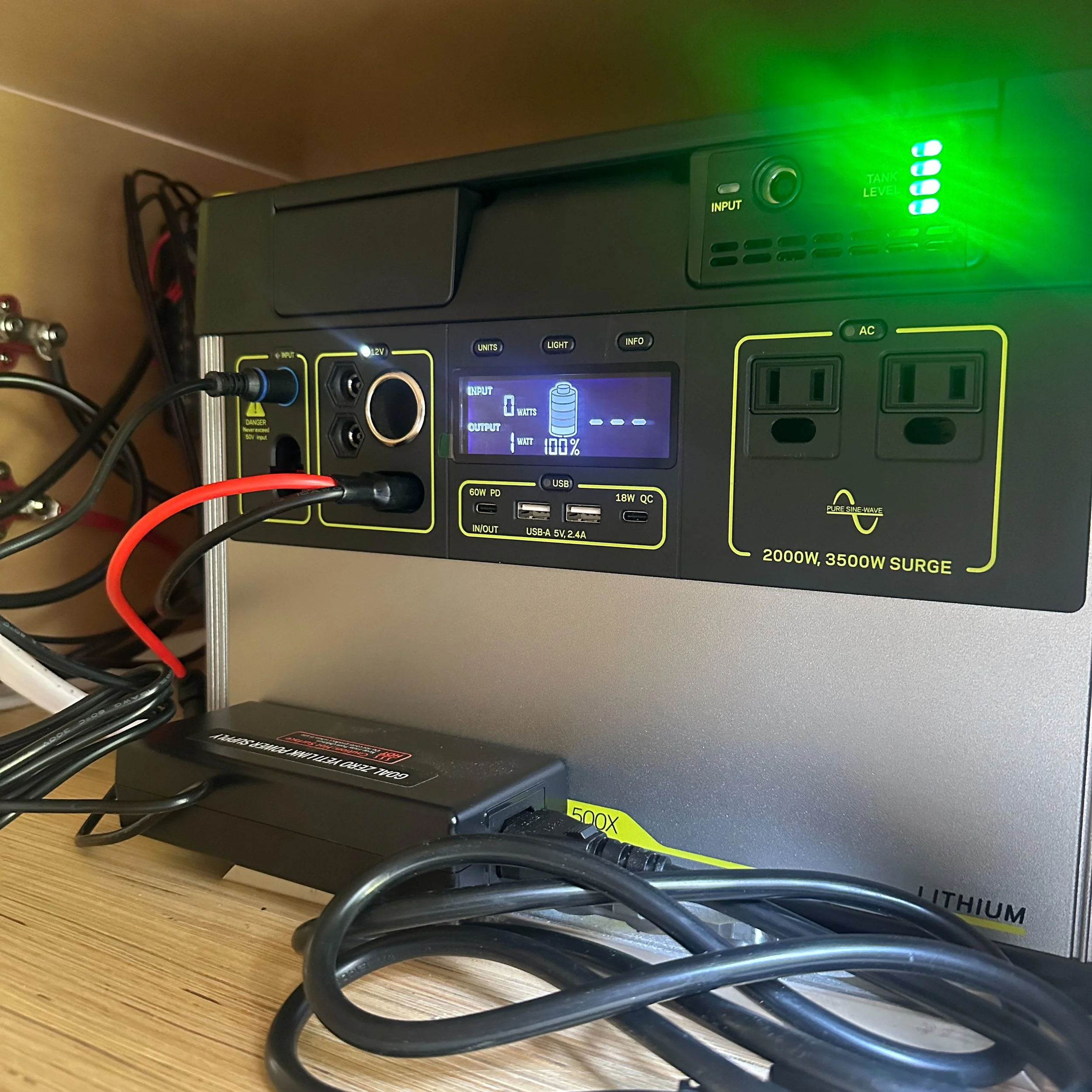 A power supply unit with multiple outlets and a digital display showing battery status, connected to various cords and devices.