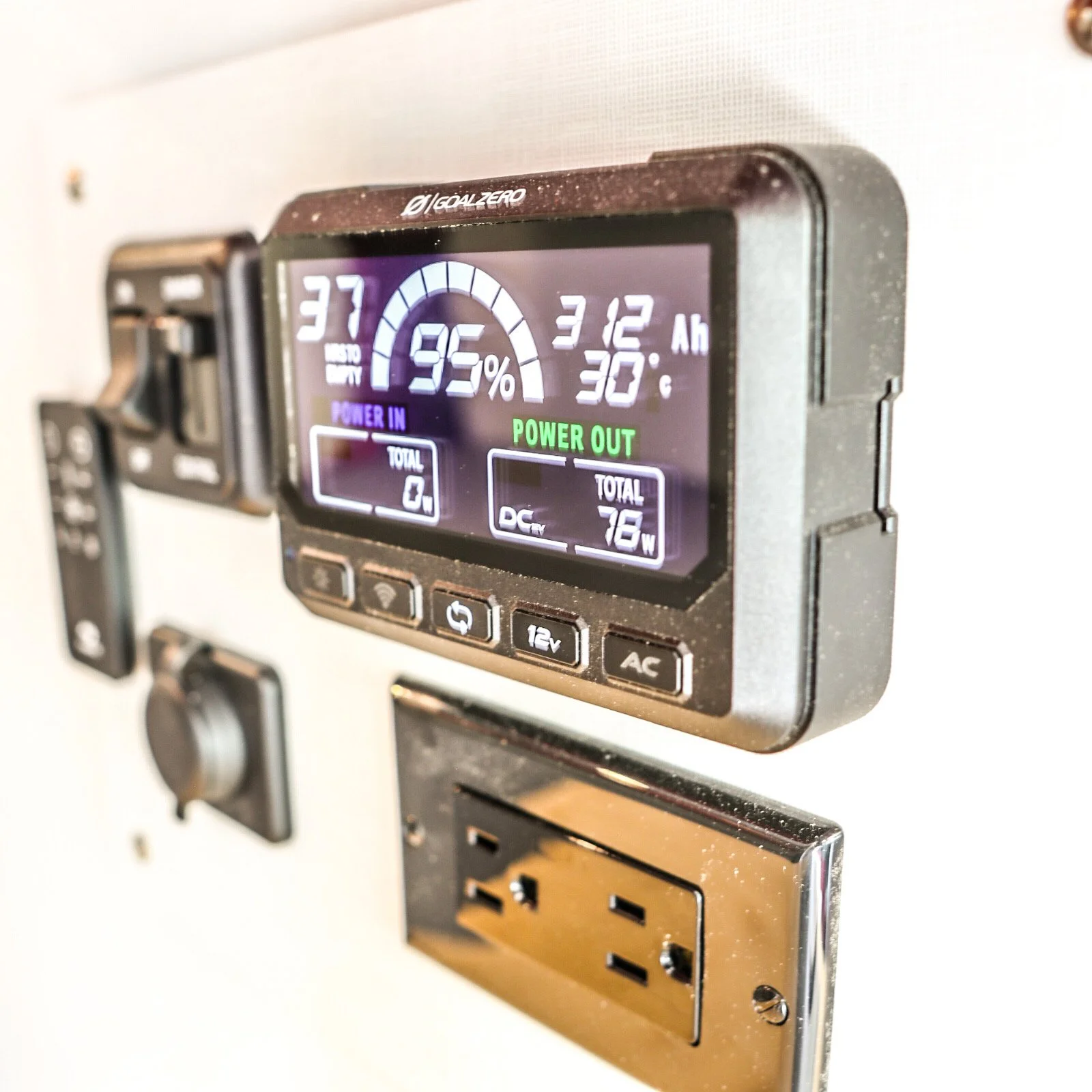 A digital control panel showing battery status at 95%, temperature at 30°C, and 3.12 Ah capacity, with options and power output details below, mounted on a wall with an electrical outlet below.