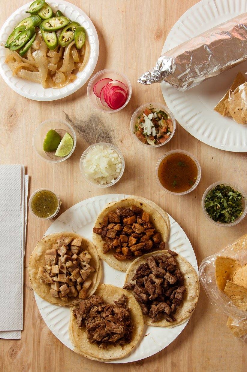 Tacos and a giant burrito wrapped in foil  surrounded by sides of salsa, radish, cilantro, lime, grilled onions and jalapeños from La Piñata in Vallejo