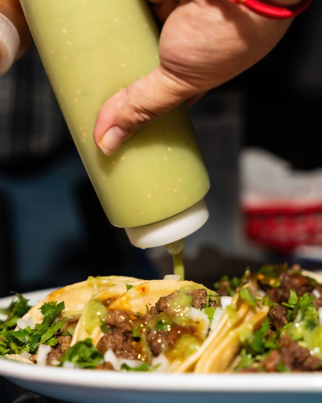 Green sauce being poured over carne asada tacos that are garnished with onions and cilantro at Taco Jalisco in Vallejo
