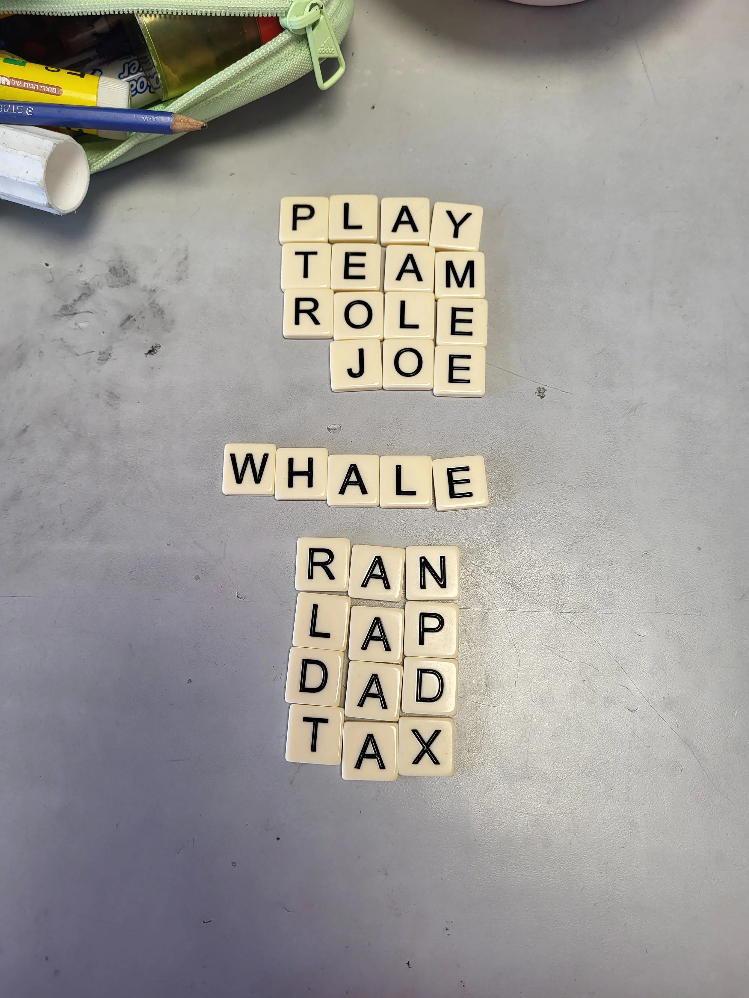 Scrabble tiles on a table spelling out phrases, with a pencil and pencil case nearby.