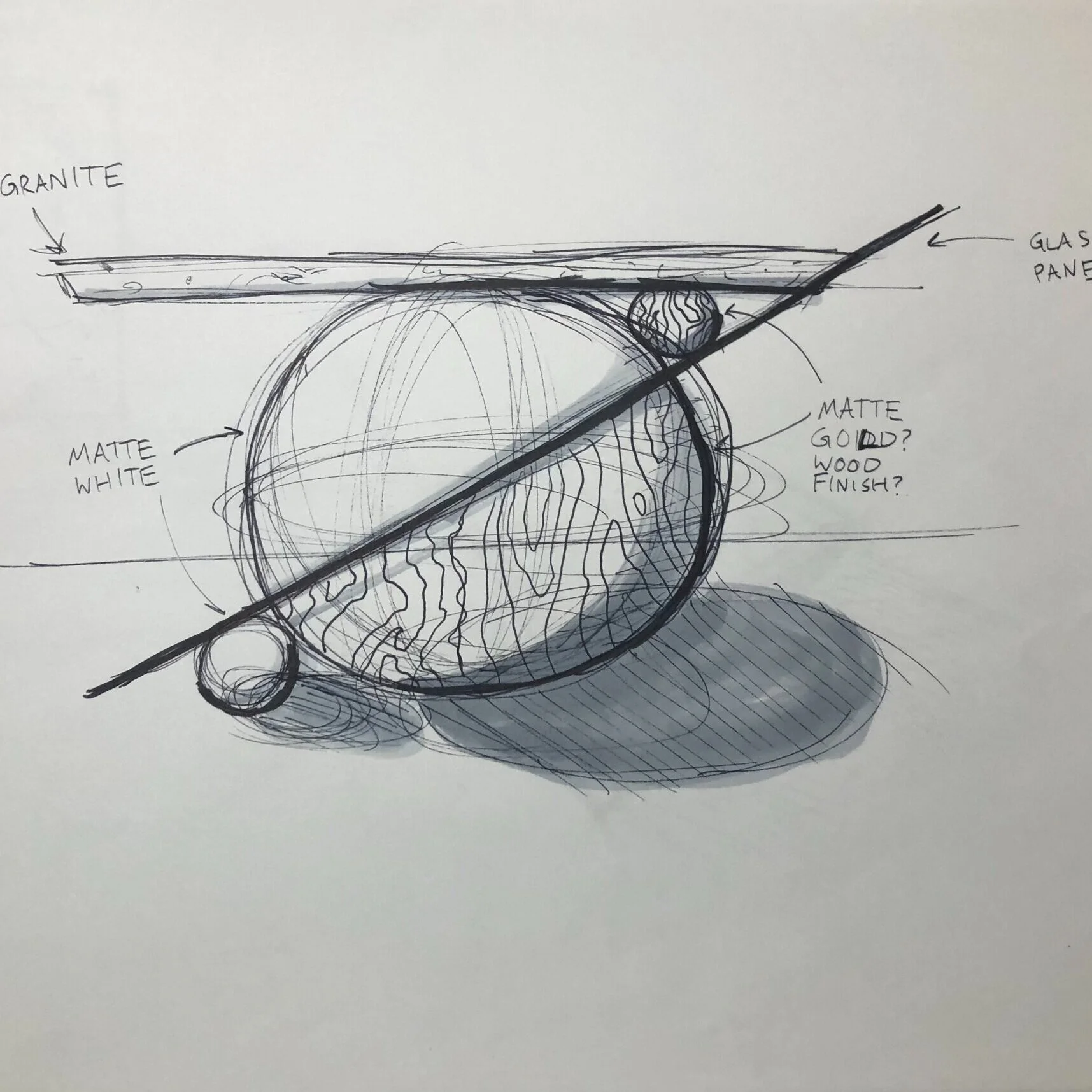 Sketch of a spherical object with layers, labeled as matte white, matte gold or wood finish, and embedded in granite, with additional small round elements and a diagonal line crossing through the object.