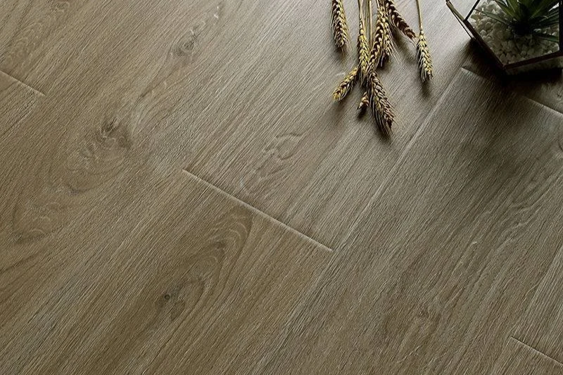 Close-up of a wood floor with some decorative dried plants and a glass container in the corner.