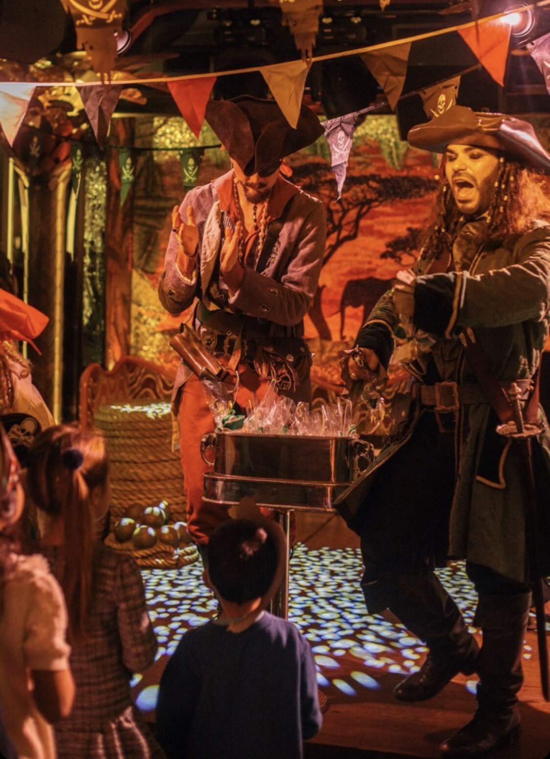 Pirate performers entertaining children in a themed setting with props and decorations.