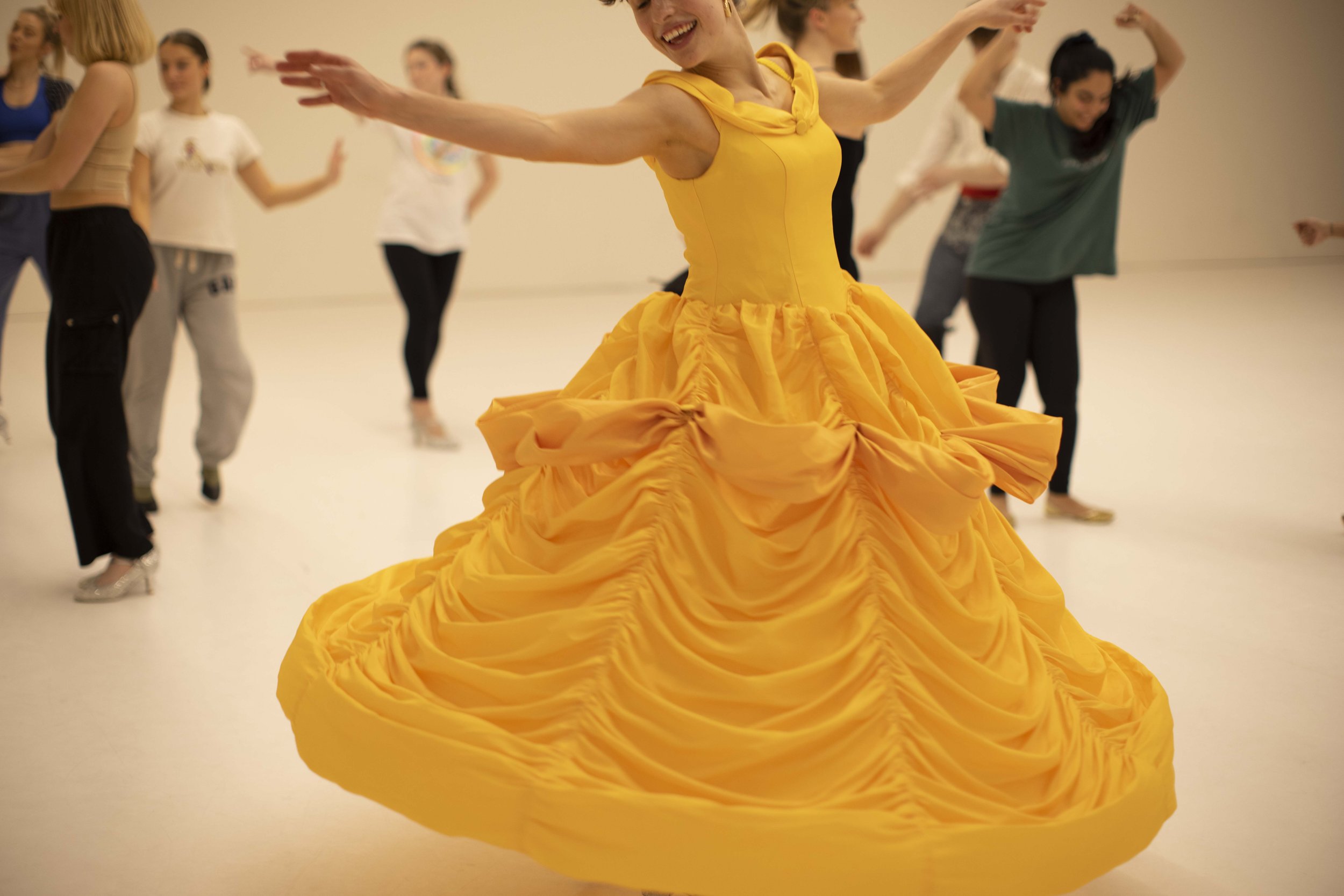 Person twirling in a yellow dress with others dancing in the background.