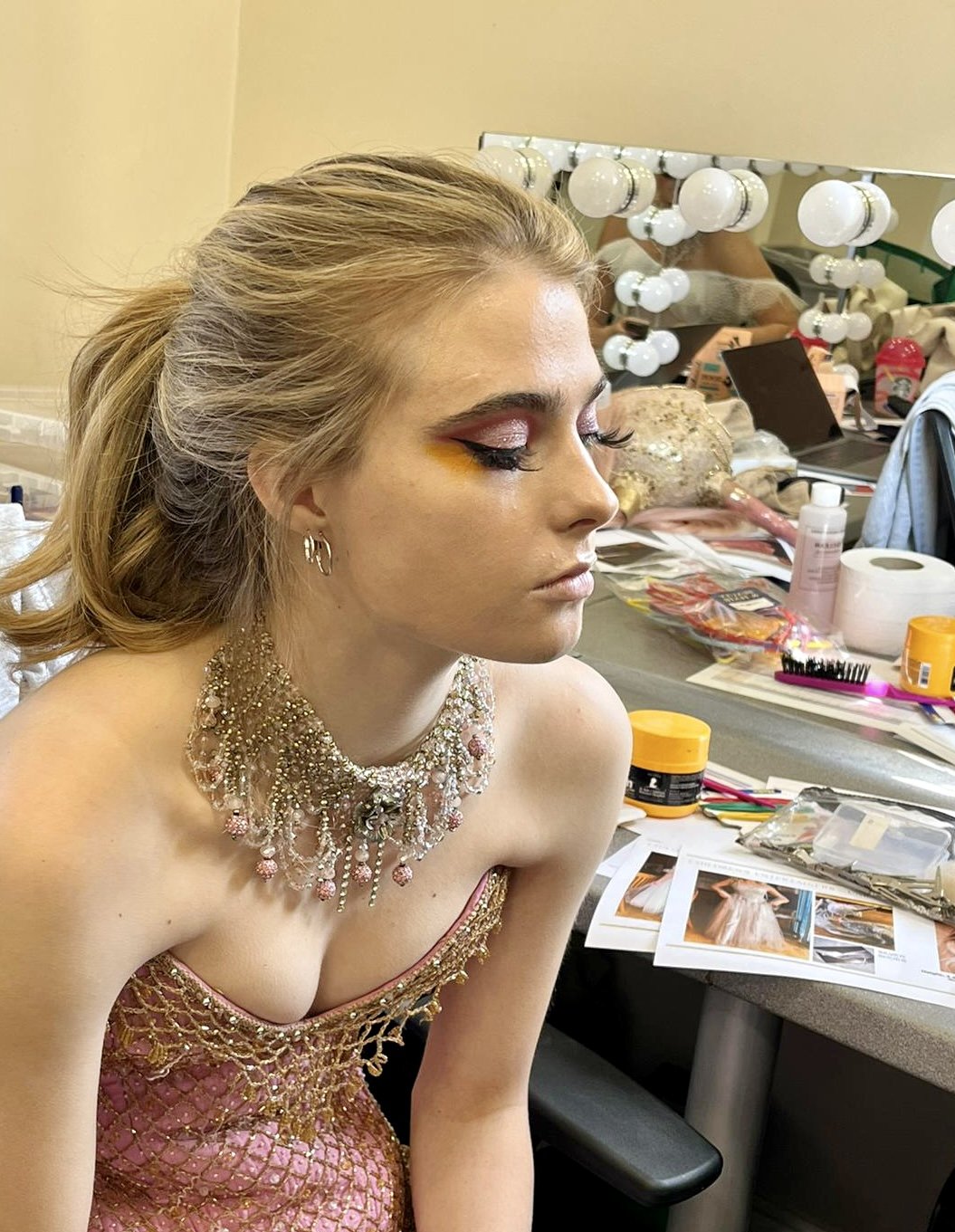 Woman wearing glamorous makeup and beaded dress in dressing room.