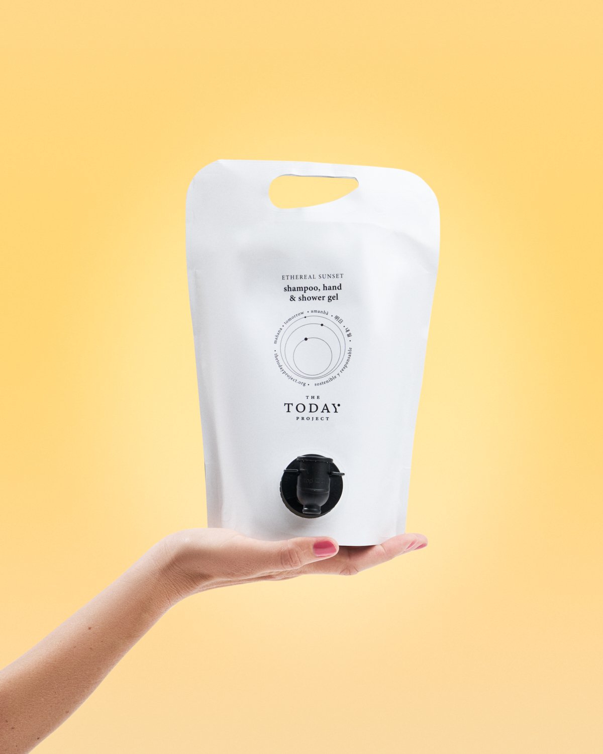 Wiederverwendbarer Beutel mit Shampoo, Hand- und Duschgel, der von einer Hand gehalten wird, vor einem gelben Hintergrund.