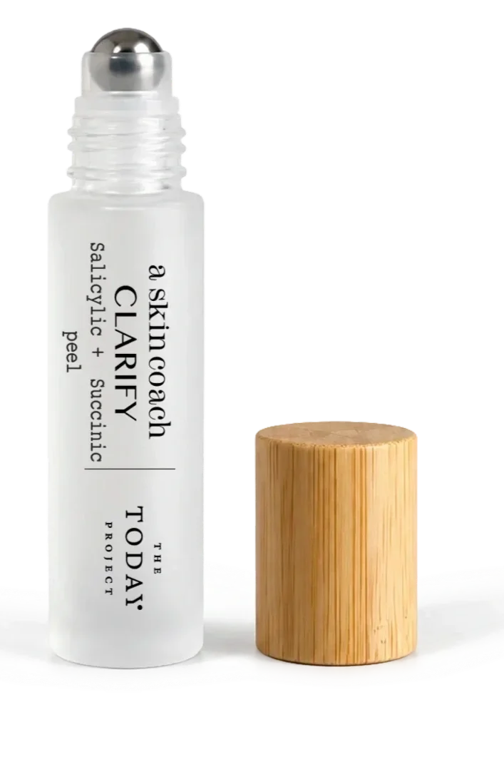 Clear skincare roller bottle with white label, black text reading 'a skin oogh CLARIFY', and wooden cap placed next to it on a white surface.