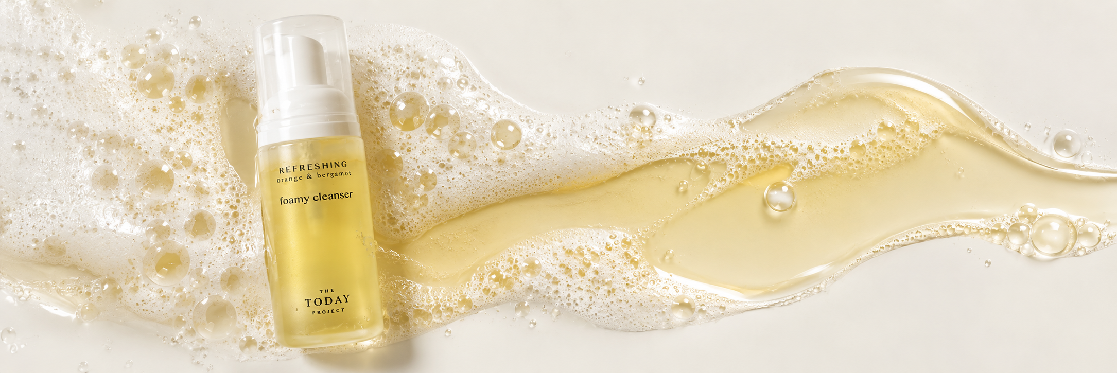 A yellow bottle of foam cleanser labeled 'Refreshing orange & bergamot' by The Today Project, surrounded by foam and liquid, with bubbles on a white surface.