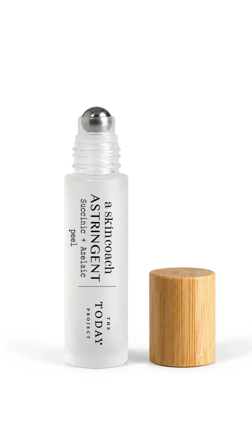 A white skincare roll-on bottle with black text reading 'A skincare ASTING EN T THE DAILY PROJECT,' next to a small wooden cap on a white surface.