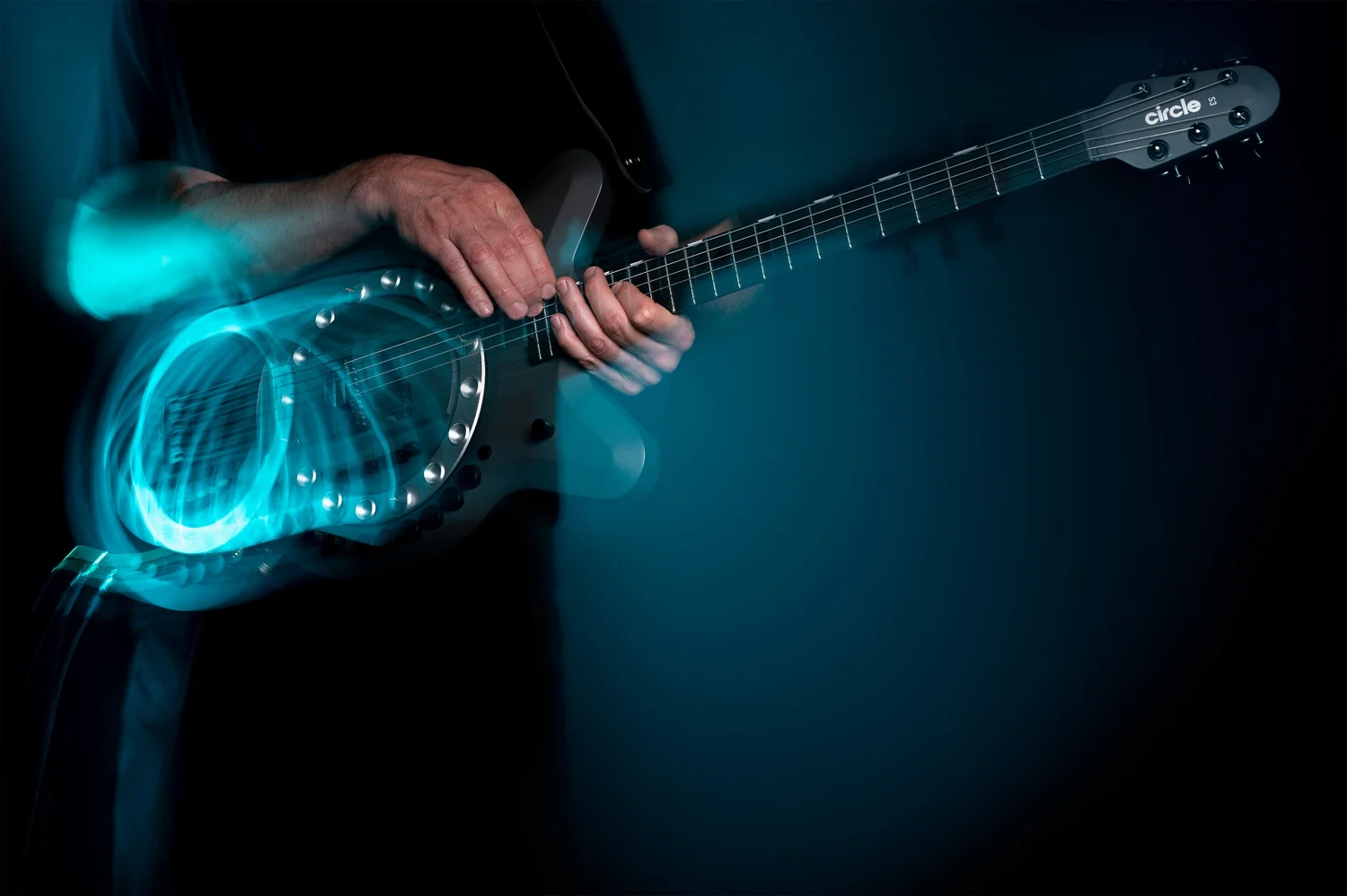 A guitarist playing a grey Circle Guitar, the wheel leaving a trail of cyan light