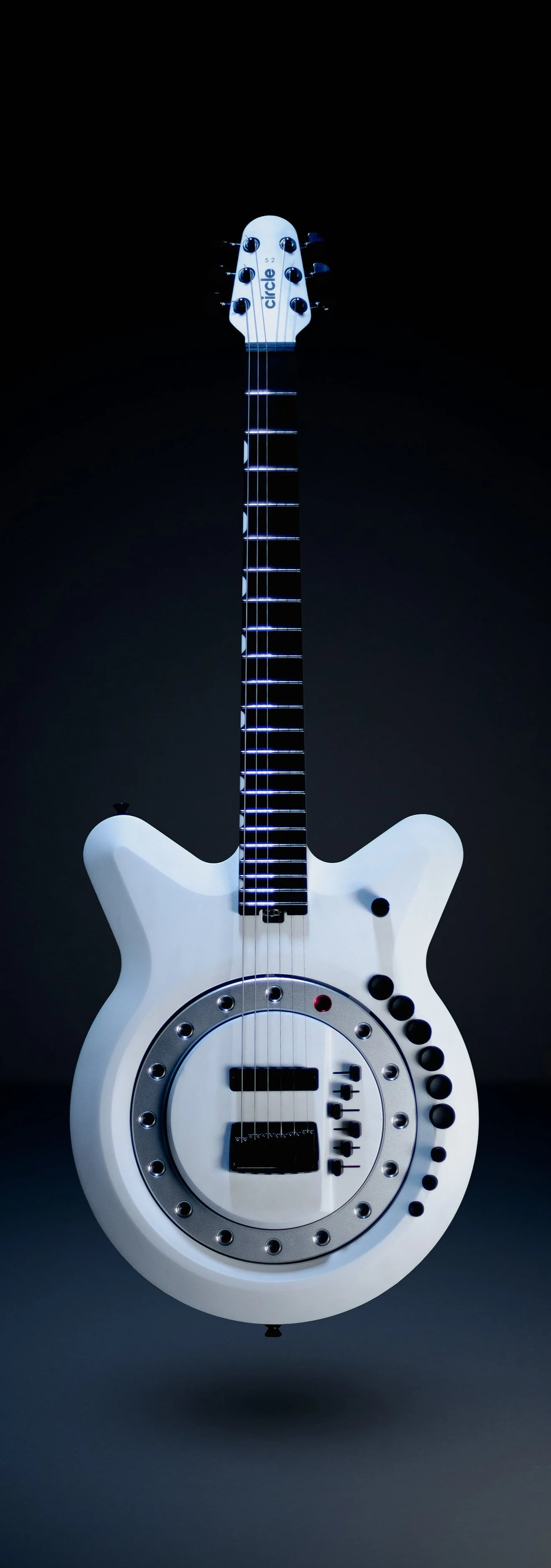 A white electric guitar with a futuristic design, featuring a circular body with a metallic ring around the sound hole and multiple black control knobs, set against a black background.