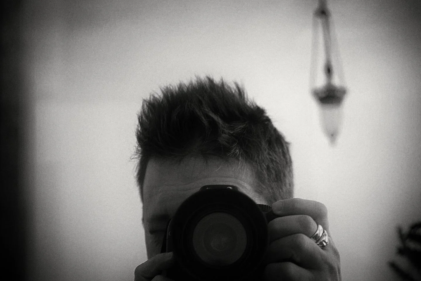 A black and white self portrait in a mirror with a big camera lens.