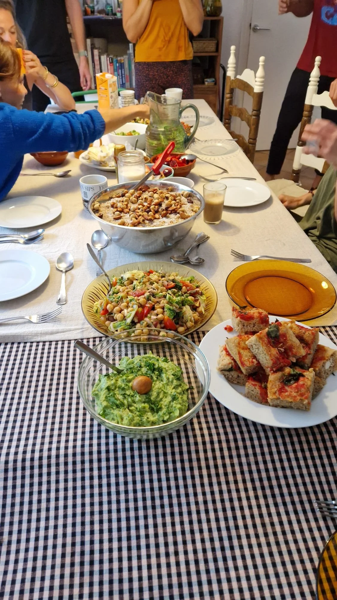 Mesa de comedor con ensaladas, pizza de pan con tomate, y una tarta de avena y frutos secos, en una reunión familiar.