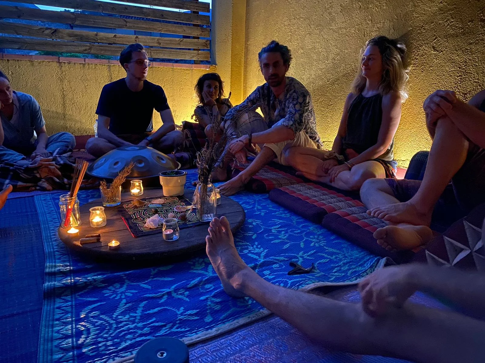 Grupo de personas sentadas en círculo en un ambiente con iluminación suave, decoraciones y velas, participando en una reunión o actividad grupal.