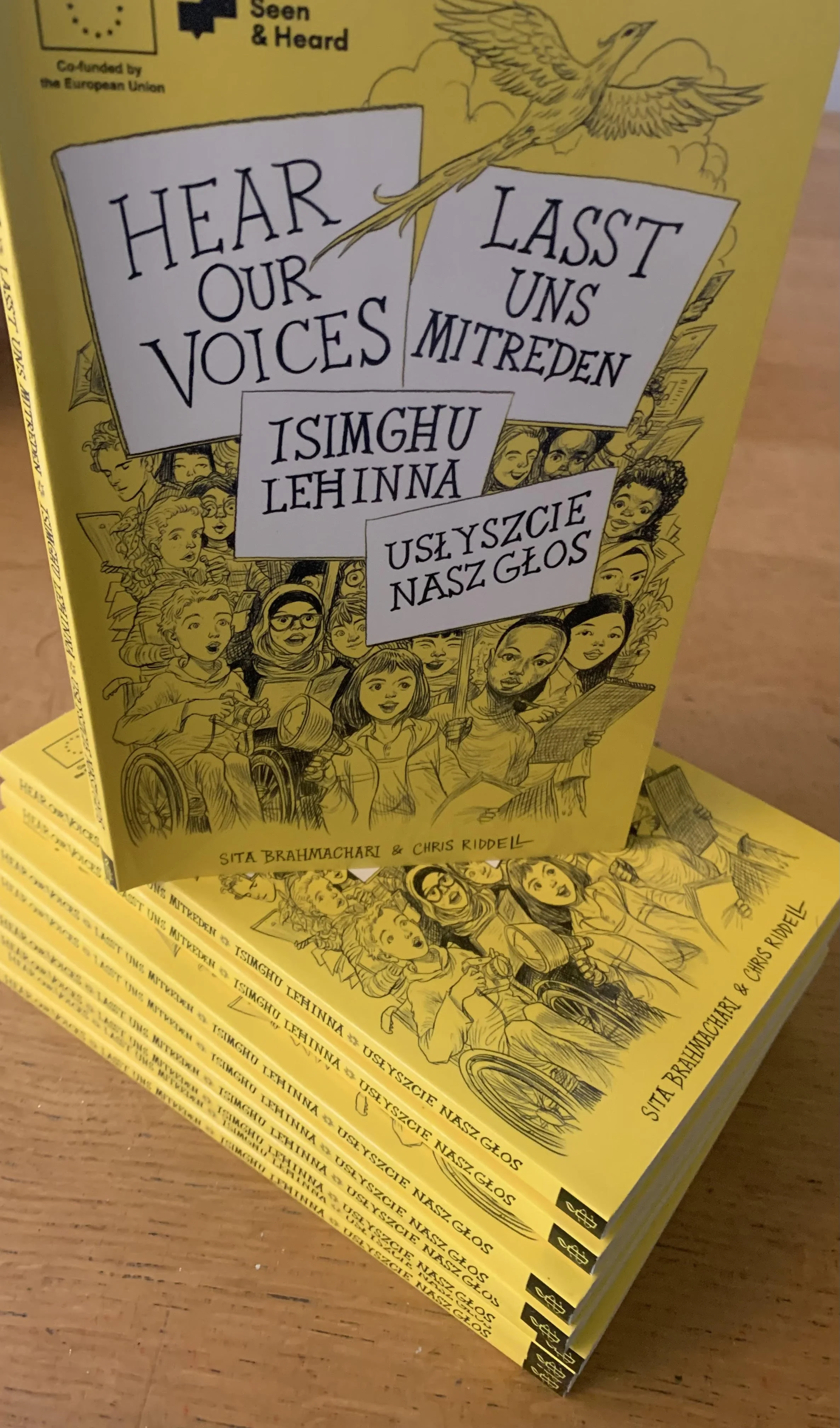 A stack of books with yellow covers called Hear Our Voices by Sita Brahmachari and Chris Riddell